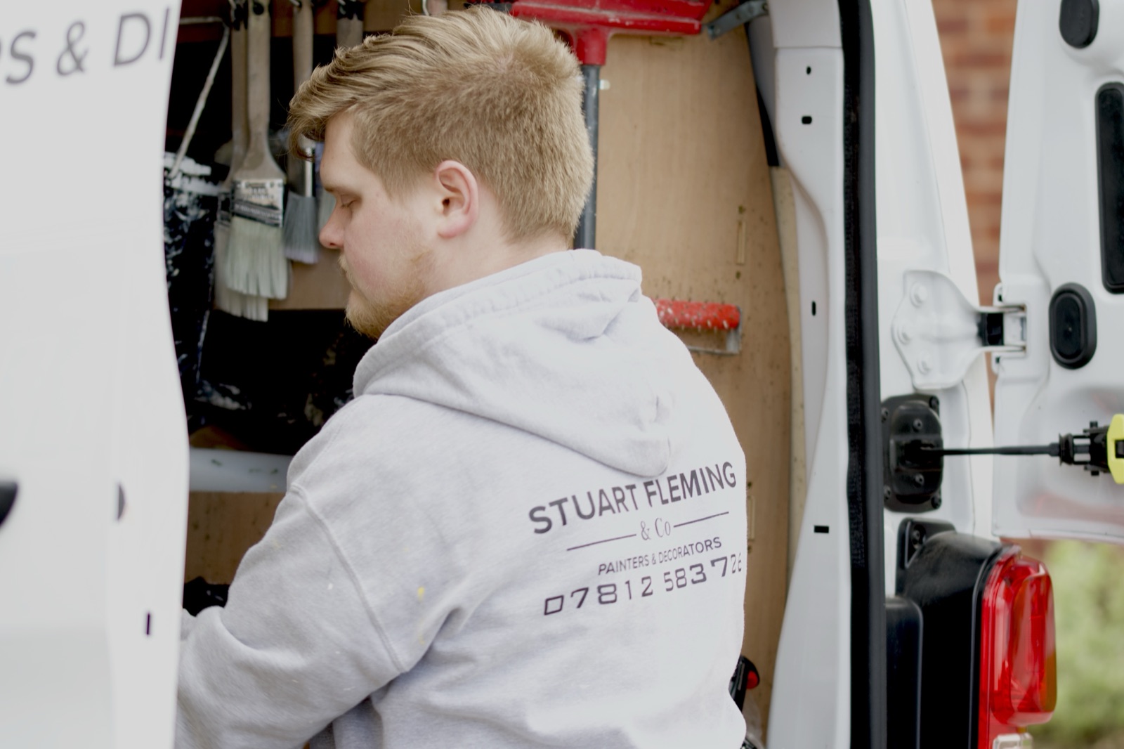 Daniel reaching for tools in the van, branded hoodie visible